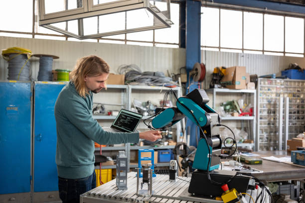 young man develops code for a robotic arm - trainee mechanic engineer student imagens e fotografias de stock