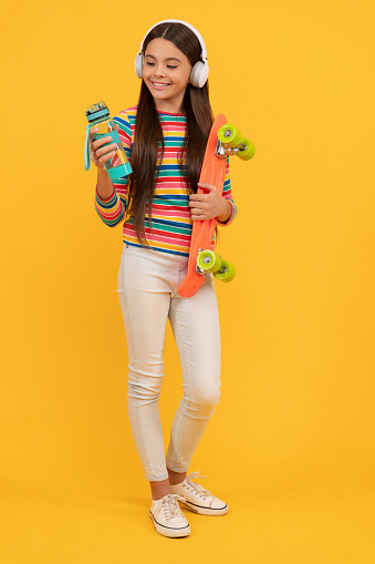 happy teen girl skateboarder listen music in headphones with penny board skateboard and sport water bottle, skater.