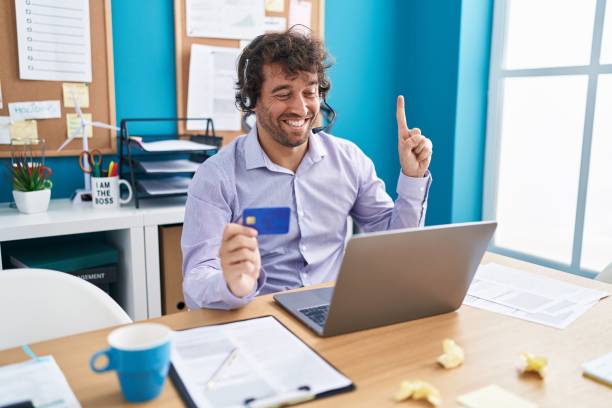 istock Hispanic young man working at the office doing online shopping smiling with an idea or question pointing finger with happy face, number one 1436395466