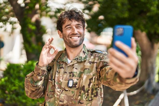 istock Hispanic young man wearing camouflage army uniform doing video call doing ok sign with fingers, smiling friendly gesturing excellent symbol 1436395487