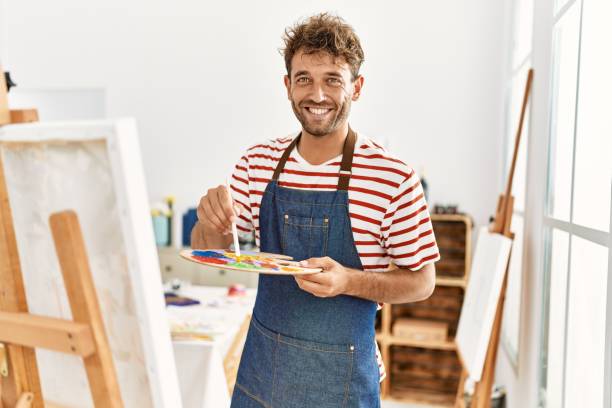 giovane ispanico sorridente che disegna fiducioso nello studio d'arte - uomo dipinge foto e immagini stock