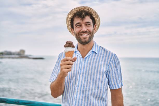 istock Young hispanic man smiling happy eating ice cream at the beach. 1436395540
