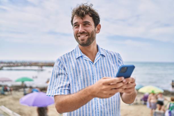 istock Young hispanic man smiling happy using smartphone at the beach 1436395548