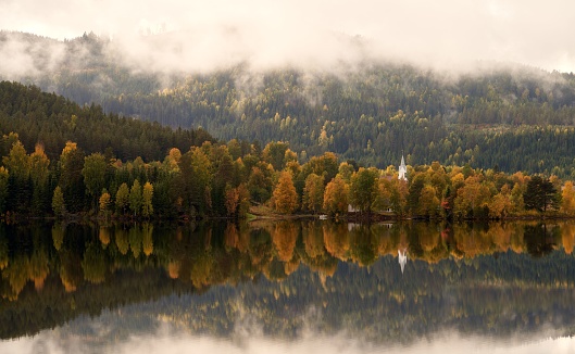 An aerial view of church surrounded by autumn dense trees and water in Norway