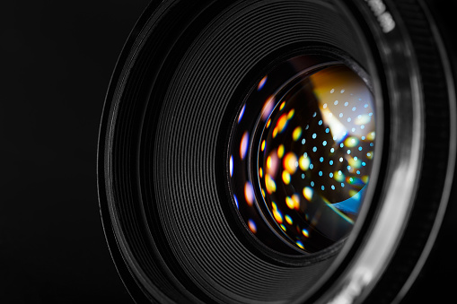 A close-up photographic lens, with multi-colored reflected spots on the surface of the front lens. Macro photography in dark style