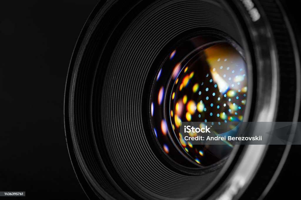 Photo lens with refraction spots close-up. A close-up photographic lens, with multi-colored reflected spots on the surface of the front lens. Macro photography in dark style Abstract Stock Photo