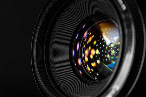 Photo lens with refraction spots close-up. A close-up photographic lens, with multi-colored reflected spots on the surface of the front lens. Macro photography in dark style aperture stock pictures, royalty-free photos & images