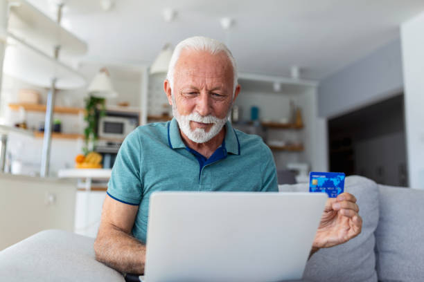 istock Mature man using laptop, holding plastic credit or debit card, senior grey haired customer making secure internet payment, shopping or browsing online banking service, entering information 1436395863