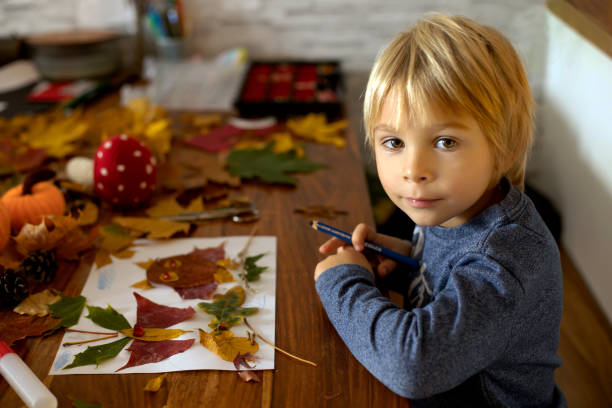 istock Child, applying leaves using glue, scissors, and paint, while doing arts and crafts at home 1436396920