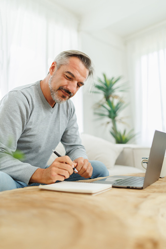 Vertical photo of Confident Bearded mature adult man writing and using laptop, Working at home office, Remote working, freelancer