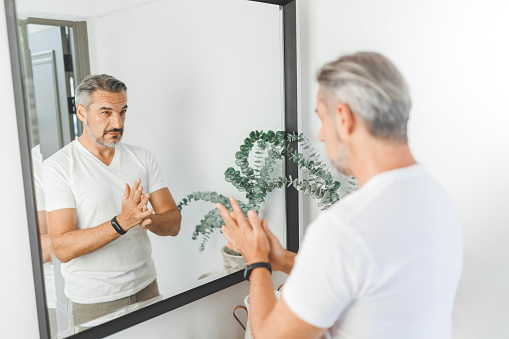 Portrait of handsome Mature adult man checking his hair and looking at his reflection in mirror