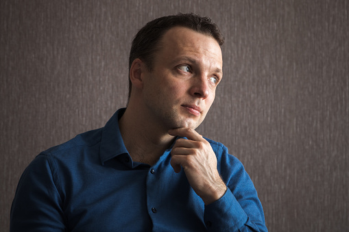 Thinking young adult Caucasian man in blue shirt, close up casual portrait with natural window light