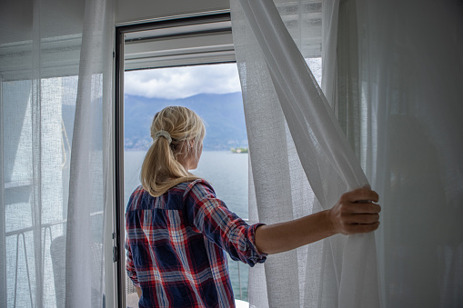 Hotel lifestyle, woman opening room curtains, lake view