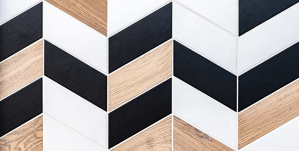 Abstract geometric pattern of different textures ceramic tiles with rhomboid shape in black and white colors and natural wood look.