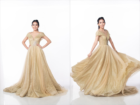 Princess wear Gold glitter Evening Gown ball dress and spin fluttering throw skirt gown around in air. 20s Asian woman dream to be princess and feel happy smile over white background isolated
