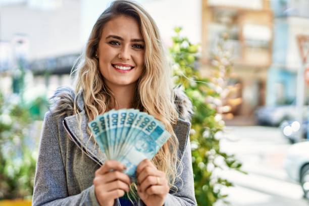 giovane donna bionda che sorride tenendo in mano le banconote reali brasiliane alla città - real people enjoyment happiness confidence foto e immagini stock