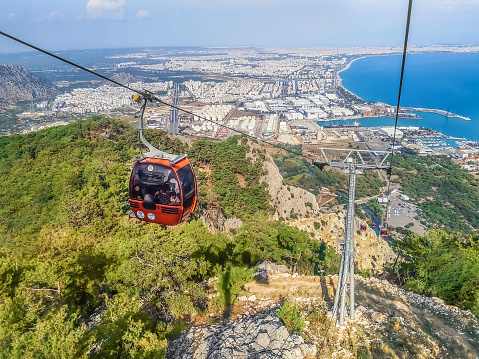 Antalya, Turkey - October 27, 2019: The orange cabin is going up the mountain on the Tunektepe Teleferik cable car against the backdrop of the Antalya panorama. Drone view of a Turkish resort town
