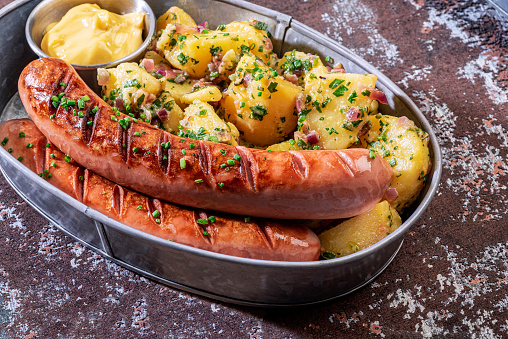 Grilled sausages, potato salad and mustard mayonnaise in a metal bowl on old wooden table.