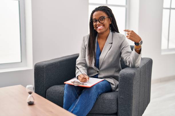 istock Young african american with braids working at consultation office looking confident with smile on face, pointing oneself with fingers proud and happy. 1436416695