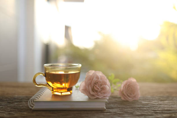 tea glass cup and pink roses head under sunlight on wooden table