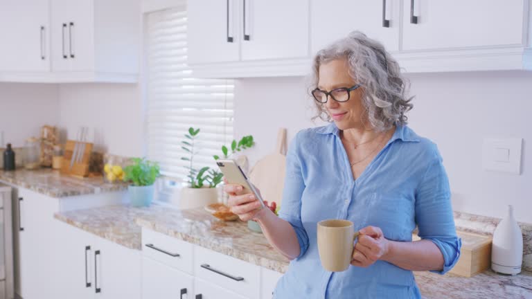 Elderly woman typing on smartphone, social media communication and check text message in kitchen. Scrolling internet network technology, tea break and relax online at home with coffee drink