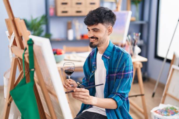 joven artista hispano bebiendo vino dibujando en estudio de arte - artists canvas beautiful art product palette fotografías e imágenes de stock