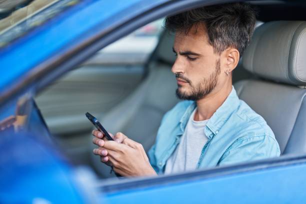 istock Young hispanic man using smartphone sitting on car at street 1436422466
