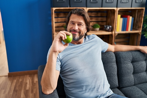 Middle age man holding apple sitting on sofa at home