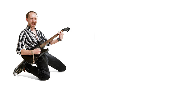 Portrait of young emotive man in stylish clothes playing guitar, posing isolated over white background. Rock musician. Concept of music, rock and roll, lifestyle, fashion. Copy space for ad, text