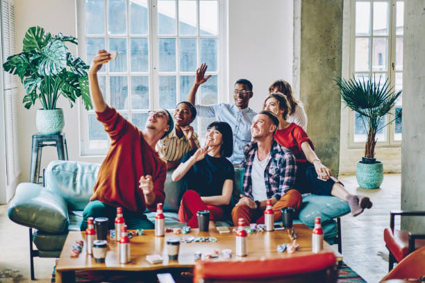 istock Satisfied hipster guys smiling at smartphone front camera while clicking selfie content via modern application for sharing media content, happy diverse friends enjoying leisure weekend for card gaming 1436424311