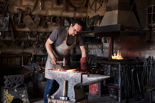 Blacksmith man, hammer and industrial anvil to mold, process or form metal, iron and steel craft construction, manufacturing and production. Handyman worker, tools and materials manual labor workshop