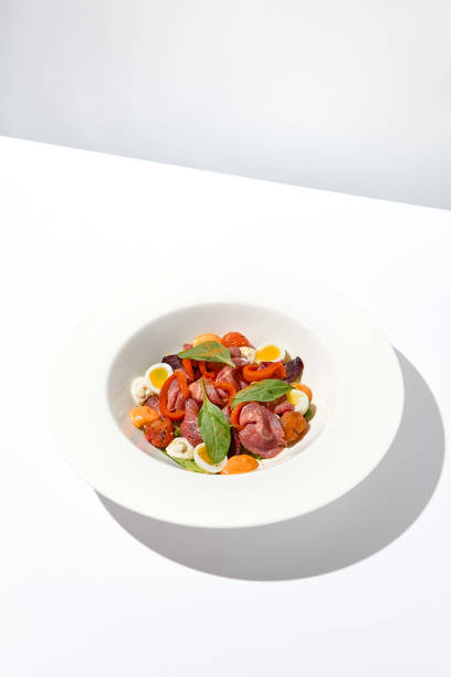 istock Salad with roast beef, vegetables and eggs on white table with harsh shadows. Steak salad in modern style with shadows of leaves. Flashy food. Meat salad with pastrami in summer menu. 1436425655