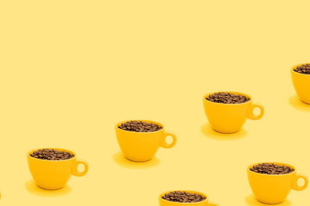 Pattern made of full cup of coffee beans with copy space on bright yellow background. Yellow mug filled with drinking energy for season break. Creative and refreshing vibrant beverage minimal concept