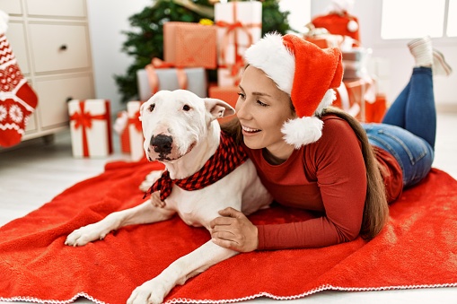 Young caucasian woman smiling confident hugging dog lying by christmas tree at home
