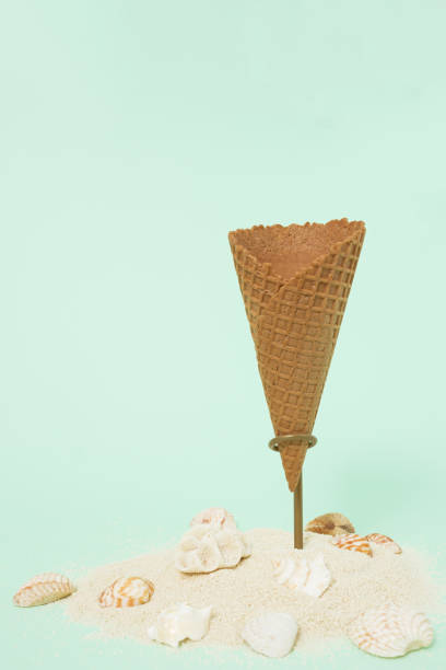 istock Ice cream cone on stand underneath decorated with sand and seashells on pastel green background. Minimal summer, vacation concept. Create layout with copy space. Waiting for fresh ice cream 1436428120
