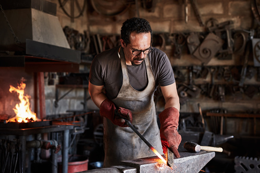 Fire, plant and industrial with a man blacksmith manufacturing a product in a metal work workshop. Industry, factory and steel with a male worker busy in a forge or foundry for production or craft