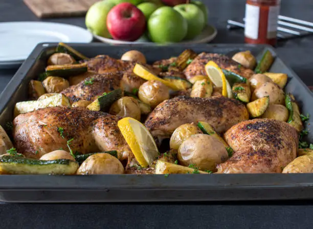 Healthy chicken meal with oven roasted chicken legs and crispy skin. Baked with potatoes and zucchini. Served on a baking sheet on kitchen table background