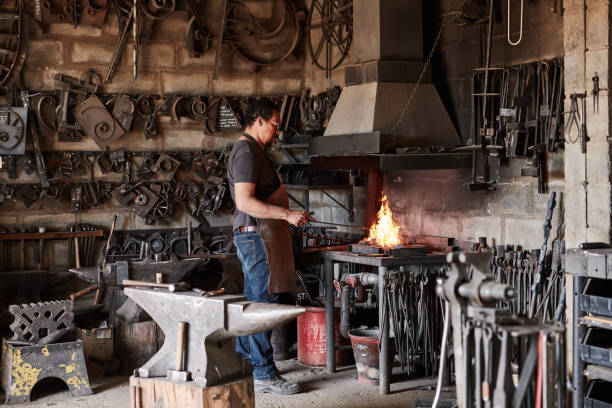 istock Man in metal workshop, blacksmith worker craftsman in forge with hammer and steel anvil welding tools in fire. Iron smith welder, melting tool and equipment working in foundry for industrial industry 1436433717