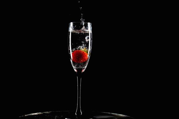 red strawberry falls into a glass with splashes on a black background stock photo