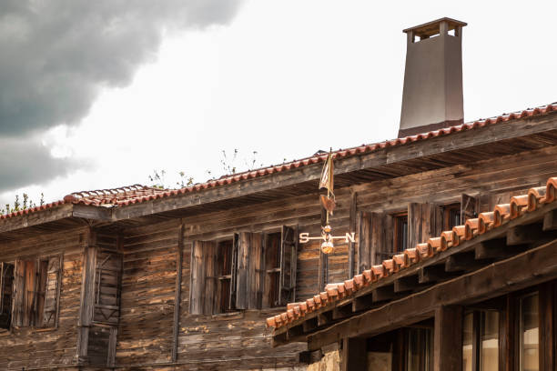An old wooden house with shutters and chimney on the roof. The weather vane is on the roof stock photo