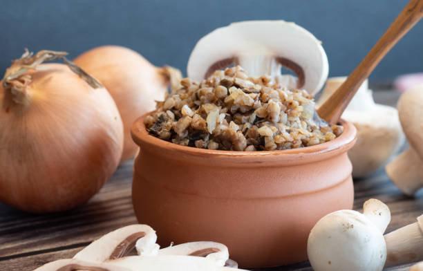 Boiled buckwheat in a pot, onion, fresh mushrooms and wooden spoons stock photo