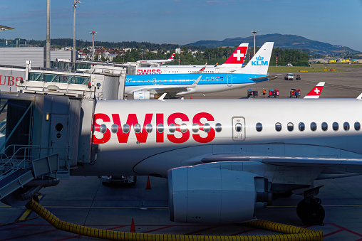 Swiss airplanes parked at Zürich Airport with air traffic control tower in the background on a sunny summer day. Photo taken August 1st, 2022, Zurich, Switzerland.