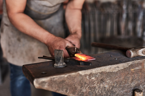 Manufacturing, creative and workshop with a man blacksmith working on design to forge in the metal industry. Designer, hands and art with a male artisan at work on steel or iron in a foundry or plant