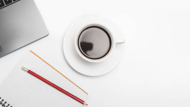 istock Coffee cup on white desk with laptop and notepad, top view 1436440043