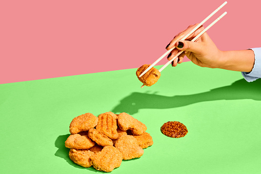 Spicy taste. Delicious image of chicken nuggets and french mustard on green tablecloth Eating with chopsticks. Food pop art. Colorful minimalism. Complementary colors