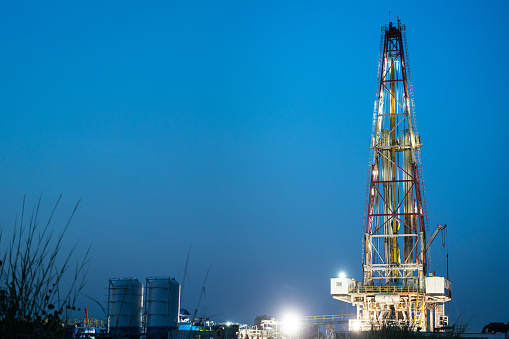 Oil field drilling rig derrick structure on dusk sky background. Industrial and business operation scene. Photo contained noise due to low light environment.
