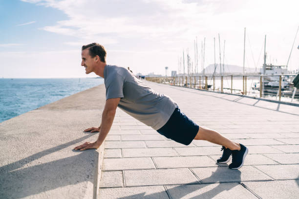 istock Determined caucasian hipster guy training in morning on coast doing push up exercises training arms, 20s positive sportsman keeping perfect body physical shape having active workout outdoors 1436444657