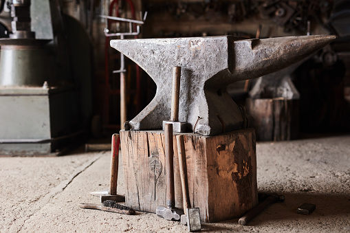 Anvil, industry and manufacturing with a hammer and tool in the foundry of a blacksmith for metal work. Workshop, product and plant with equipment on a floor of a forge for art, craft or metalworking