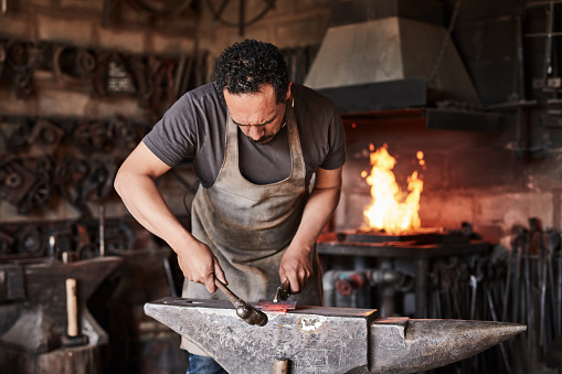 Blacksmith, hammer and man with anvil for metal, tools or knife in workshop. Industry, steel and iron in foundry, smithy or workplace with design of alloy, weapon or sword in industrial factory