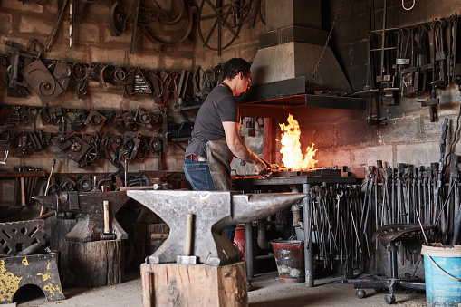 Blacksmith, metal and workshop with heat, industry and melting steel for design, manufacturing and work. Industrial, forge and job in factory with tools, iron and alloy while working at foundry
